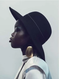 Profile portrait of a Black woman wearing a black wide-brimmed hat, large gold earrings, and a white top
