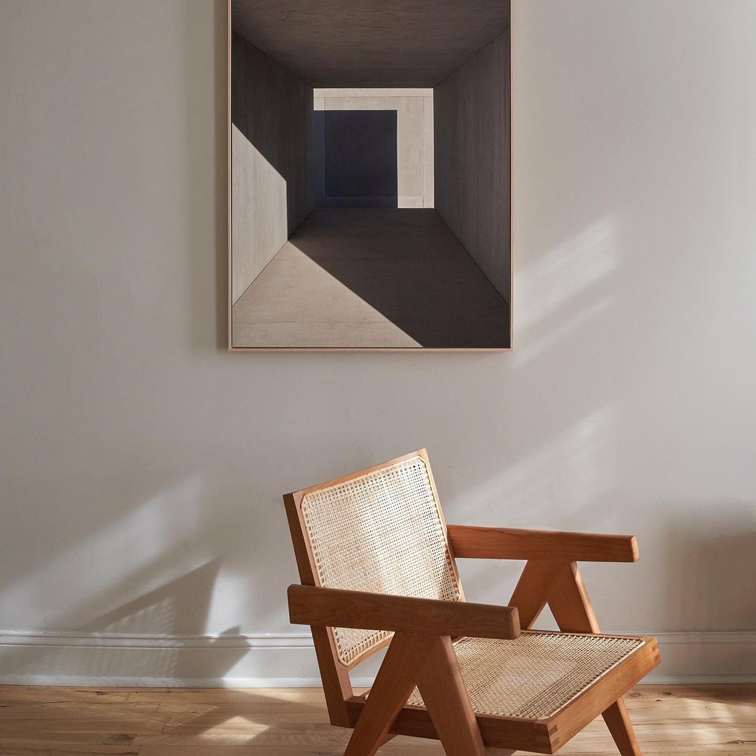 Interior design featuring a wooden chair in front of wall art depicting a concrete hallway with geometric shadows and stark lighting.