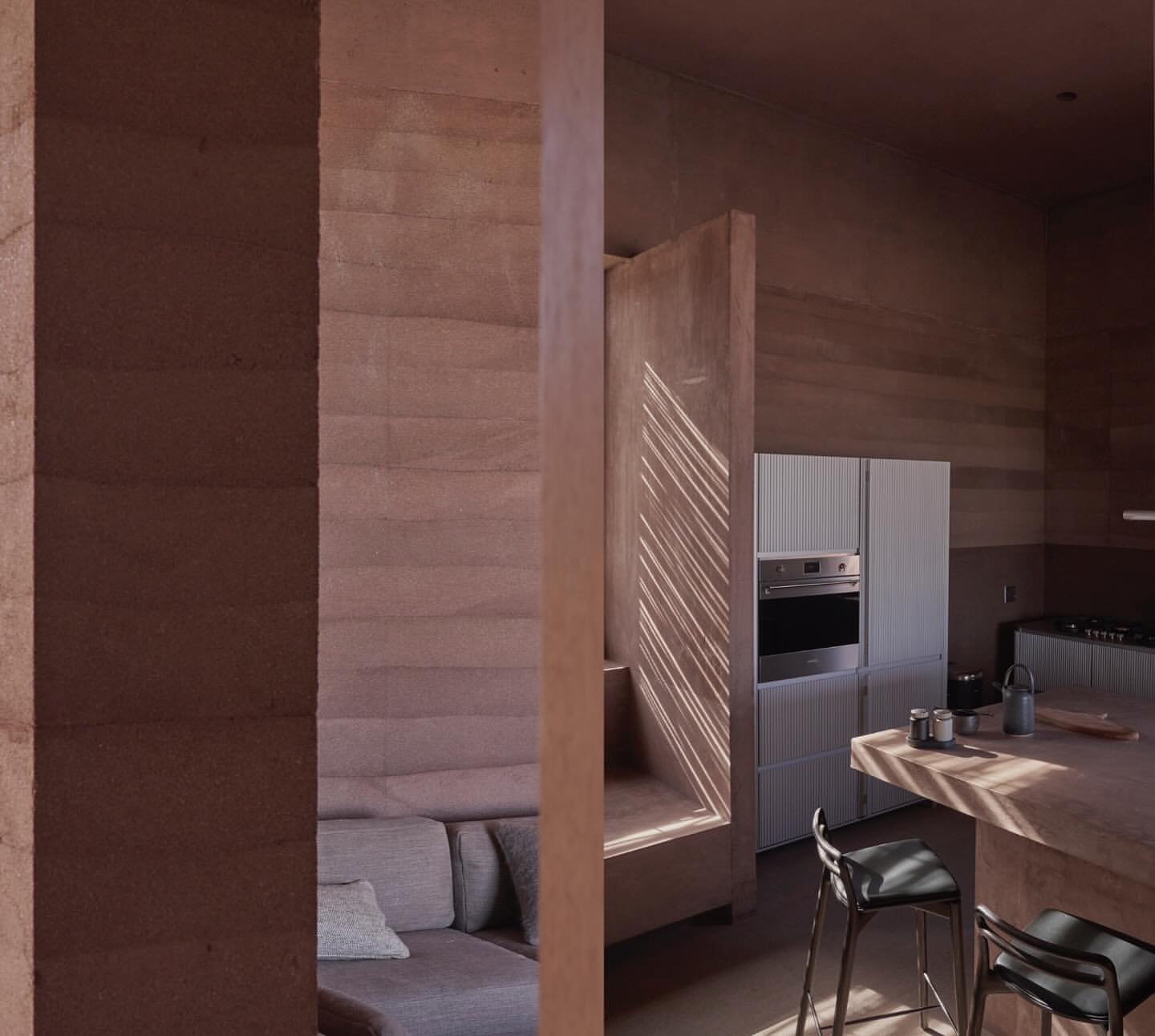 Interior view showcases a couch and open-concept kitchen with light streaming through window, highlighting neutral tones and minimalist design.