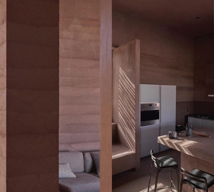 Interior view showcases a couch and open-concept kitchen with light streaming through window, highlighting neutral tones and minimalist design.