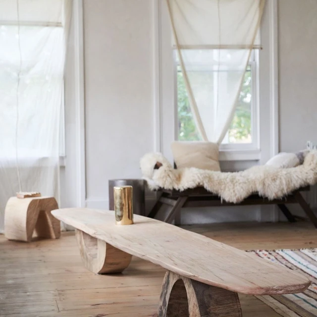 Minimalist living room interior featuring a long, light-wood coffee table, stool, and daybed with neutral tones, soft lighting, and wooden floors.