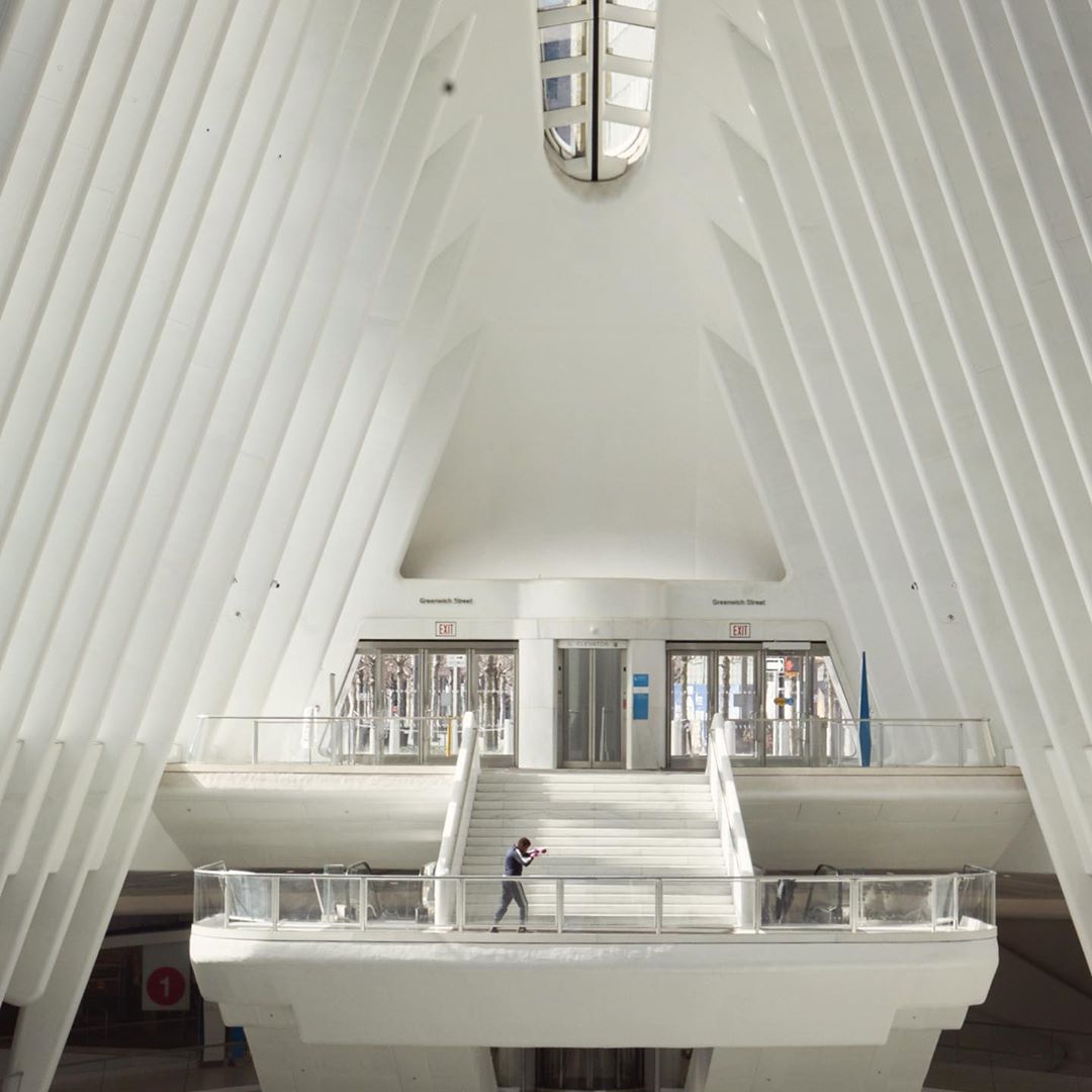 Person stands in the white Oculus transit hub in New York City, featuring ribbed walls and a distinctive architectural style, bathed in sunlight.