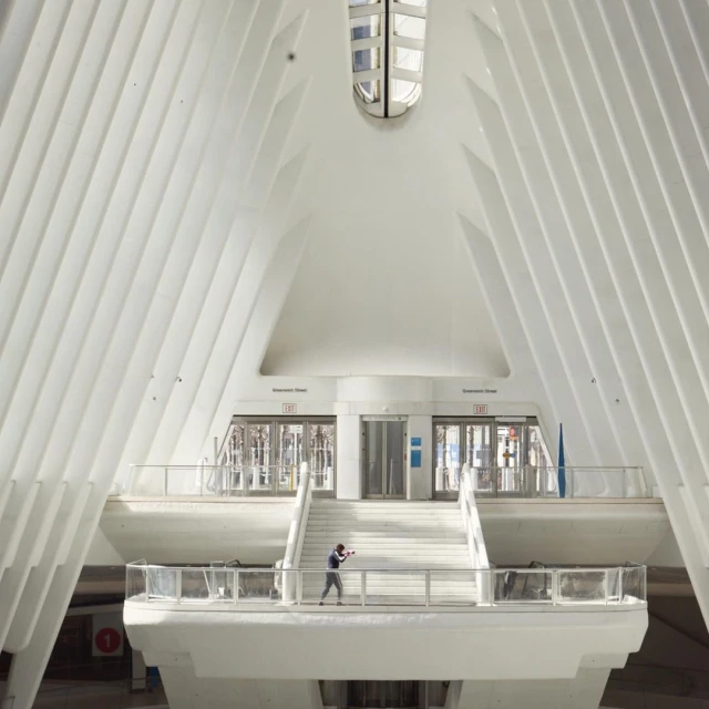 Person stands in the white Oculus transit hub in New York City, featuring ribbed walls and a distinctive architectural style, bathed in sunlight.