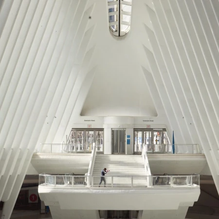 Person stands in the white Oculus transit hub in New York City, featuring ribbed walls and a distinctive architectural style, bathed in sunlight.