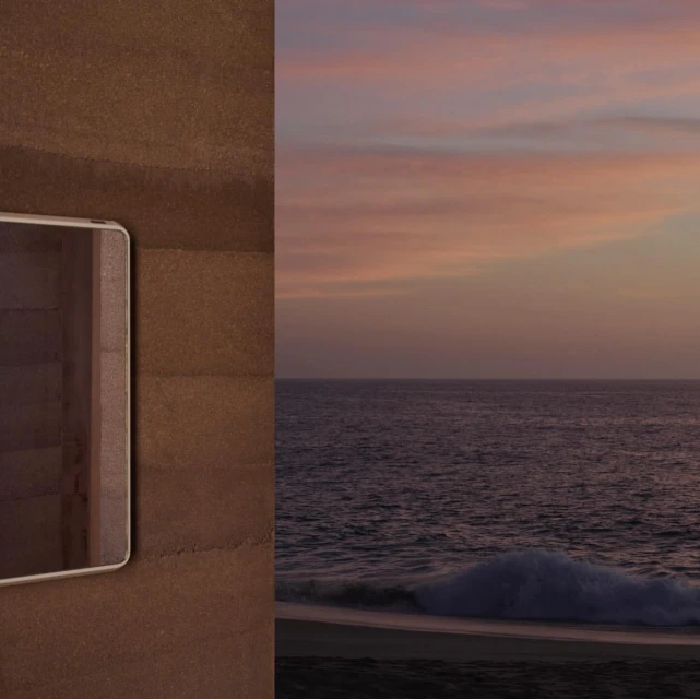 Open tablet lying on brown textured surface beside an ocean scene at sunset, featuring calm waters and soft, colorful sky.