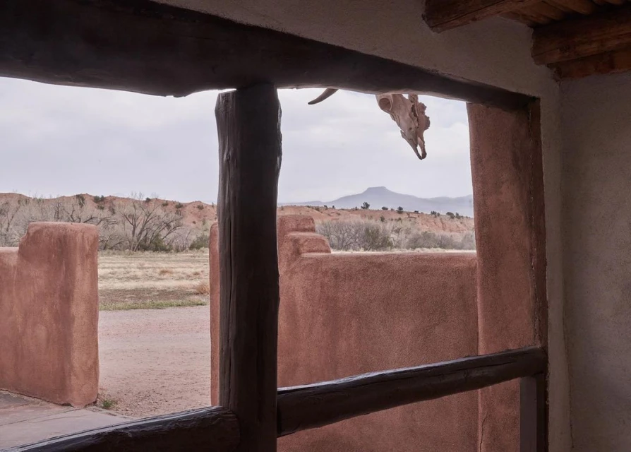 Adobe home with wooden beams frames a view of a mountain in the distance and a cow skull hanging above the doorway.