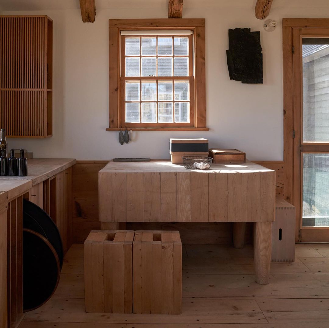 Interior featuring a wooden table with boxes and shells, complemented by rustic wood floors, cabinetry, and a sunlit window.