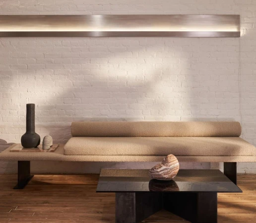 Textured beige daybed against a white painted brick wall with a long horizontal light fixture and a dark coffee table