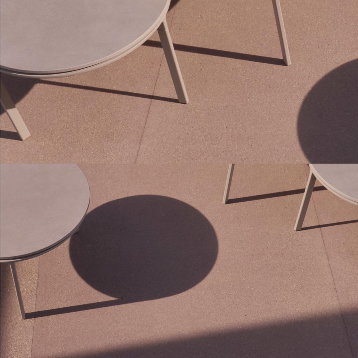 Overhead shot of two round tables casting shadows on a textured tan surface, creating a minimalist and geometric composition.