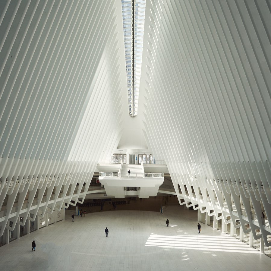 Architectural shot of the World Trade Center Transportation Hub in New York City featuring the interior and the structure, with several people.