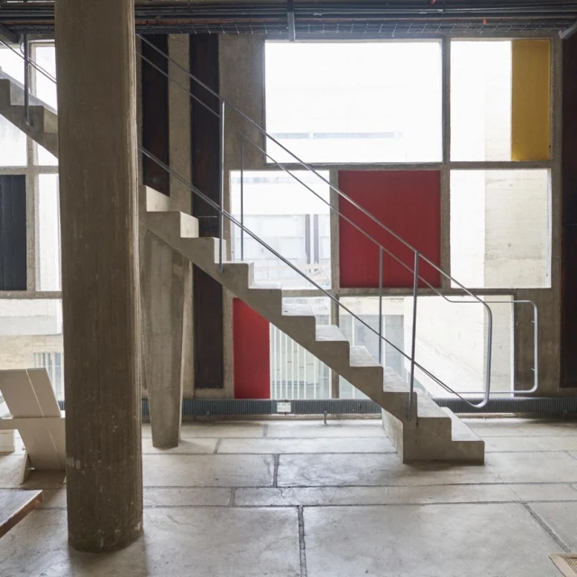Interior space with concrete stairs and pillars, featuring a window with yellow, red, black, and clear glass panes.