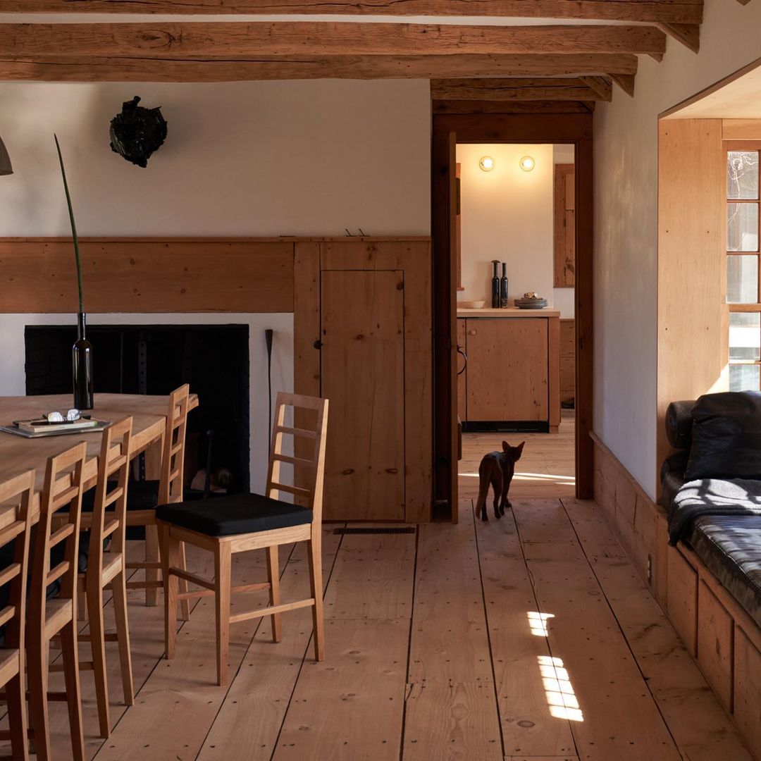 Warmly lit home interior with wooden table and chairs, dog walking through doorway, and rustic wood details.