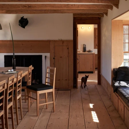 Warmly lit home interior with wooden table and chairs, dog walking through doorway, and rustic wood details.