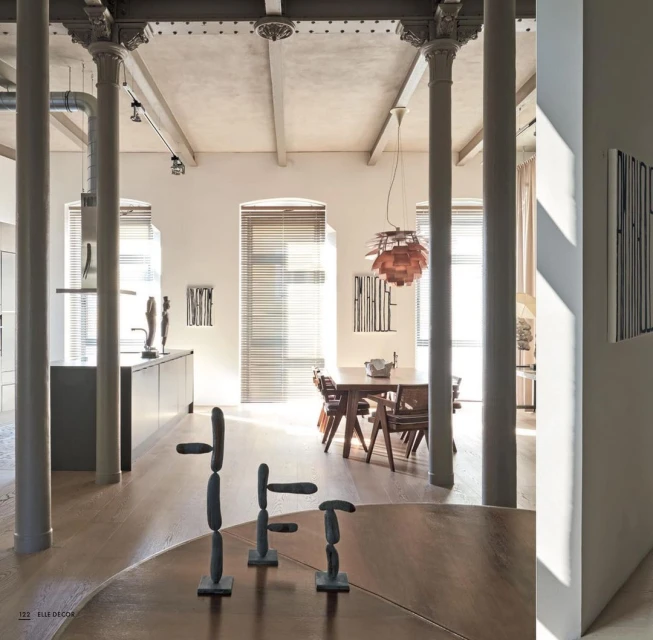 Interior view of a modern living space showcasing a dining table, chairs, artwork, and minimalist sculptures on a round wooden table.