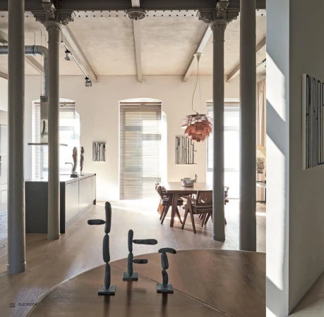 Interior view of a modern living space showcasing a dining table, chairs, artwork, and minimalist sculptures on a round wooden table.