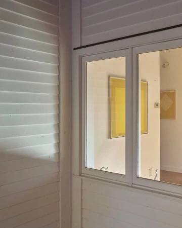 Interior view featuring a white-framed window, shuttered wall, and framed art, capturing a blend of architectural elements and artistic display.