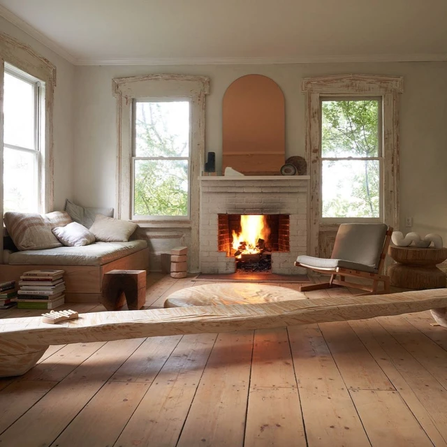 Sun-drenched living room with fireplace, lounge area, and light wood floors. Large windows offer outdoor views and natural light.