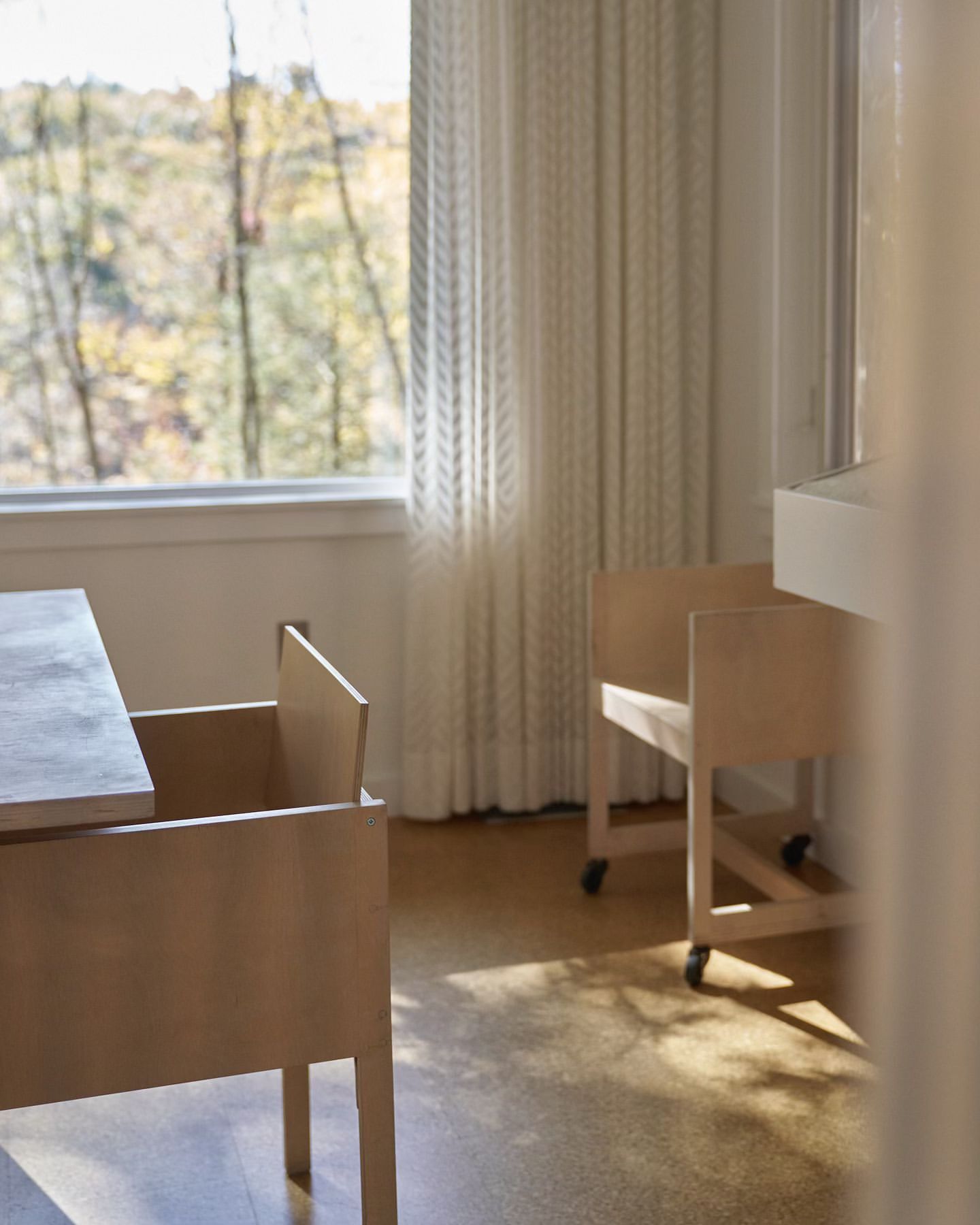 Beige-toned interior with furniture in minimalist style, featuring a table and chairs with a view of trees through a window.