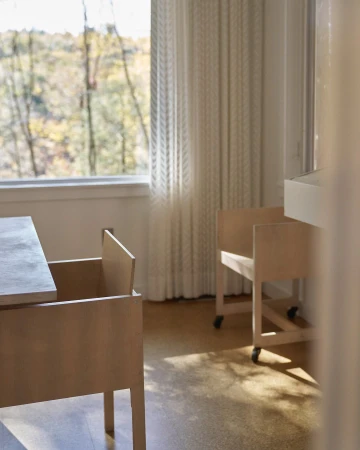 Beige-toned interior with furniture in minimalist style, featuring a table and chairs with a view of trees through a window.