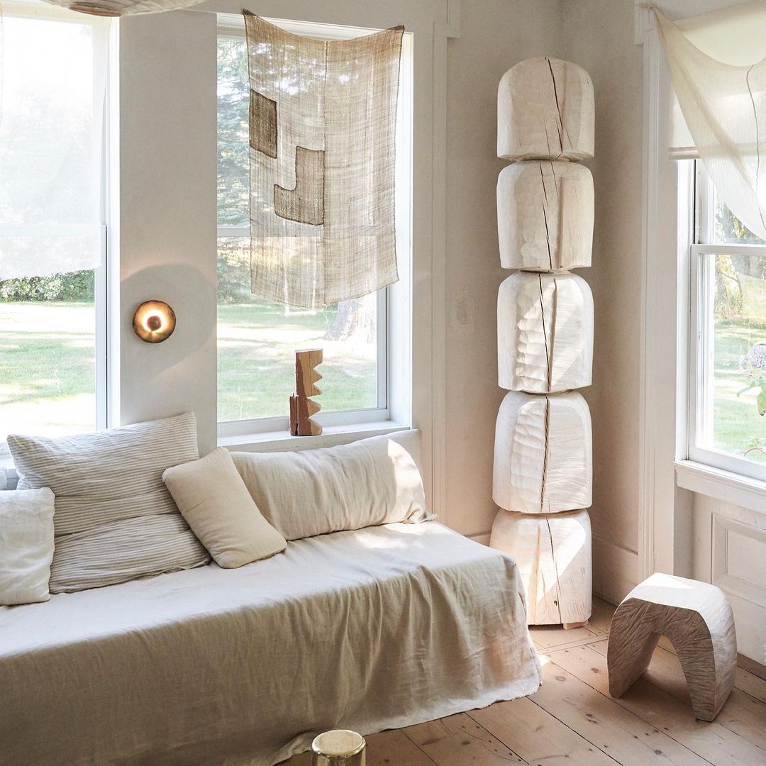 Interior of a living room with a daybed, wooden sculpture, and decorative wall hanging, emphasizing minimalist and natural design elements.