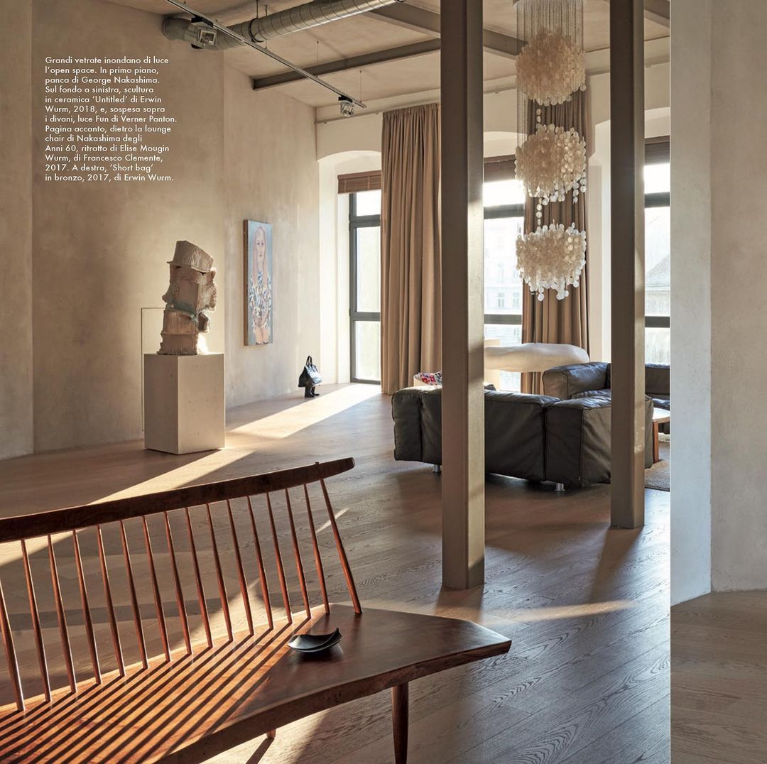 Living room interior with a wooden bench in the foreground, a sculpture on display, a lounge area, and decorative lighting.