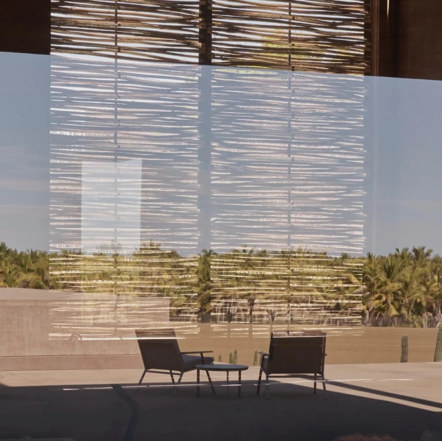 Outdoor lounge area with two chairs and a table on a patio, palm trees in background, muted color palette and modern design.