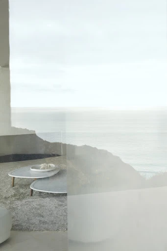 Minimalist home interior view of a hillside with ocean view, light grey color palette, two triangle-shaped coffee tables, and soft natural light.