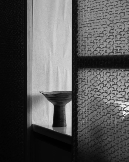 Monochrome studio shot of a dark vase on a ledge against a textured background, captured in a vertical composition with artful lighting.