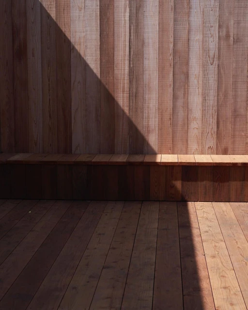 Angled view of a wood wall and deck with light and shadow creating triangular patterns; minimalistic.