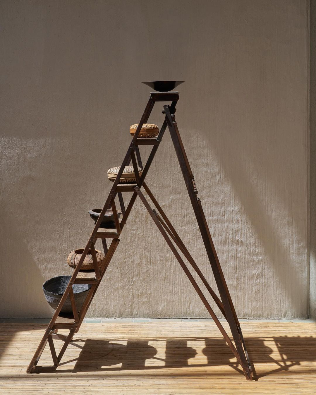 Rustic ladder shelf displaying bowls and baskets in a sunlit interior, creating a minimalist and organic home decor arrangement.