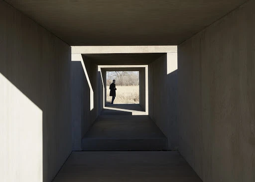 A person standing inside a rectangular concrete tunnel framing a view of a grassy field, captured by Martien Mulder.