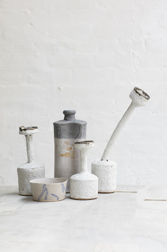 Still life featuring a collection of ceramic vases and a bowl with a leaf design, set against a textured white background.