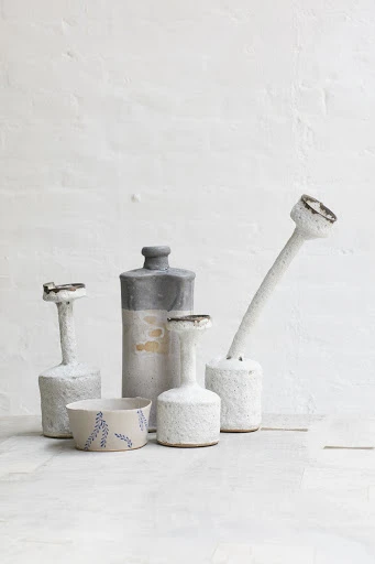 Still life featuring a collection of ceramic vases and a bowl with a leaf design, set against a textured white background.