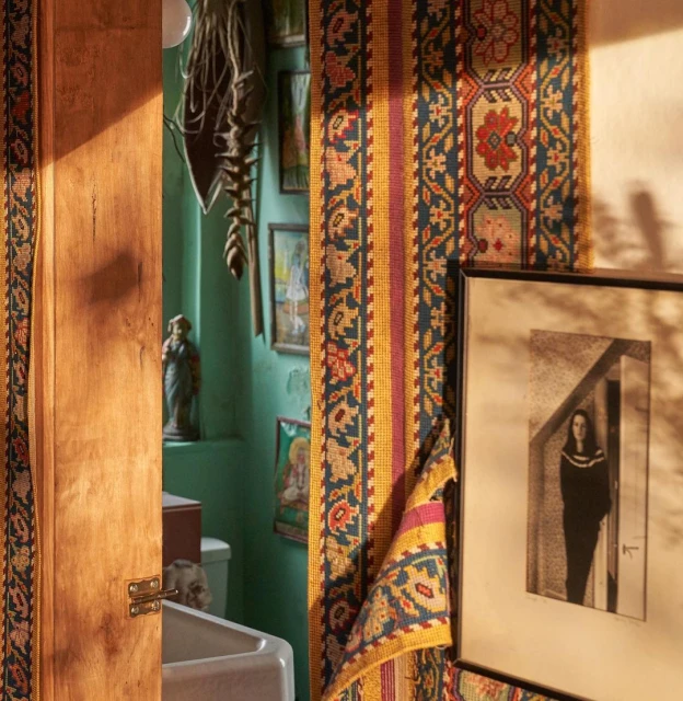 Warm-toned, eclectic interior featuring a textured rug fragment, framed monochrome art, and a glimpse into a teal-painted room, creating a cozy, vintage aesthetic.