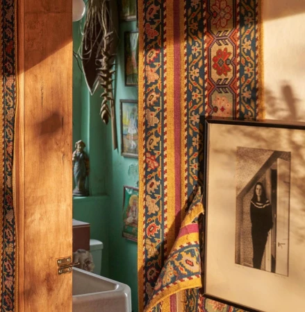 Warm-toned, eclectic interior featuring a textured rug fragment, framed monochrome art, and a glimpse into a teal-painted room, creating a cozy, vintage aesthetic.