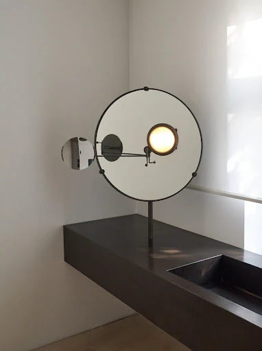 Modern bathroom interior featuring a round mirror with an integrated light, mounted above a sleek, dark-colored vanity with a sink.