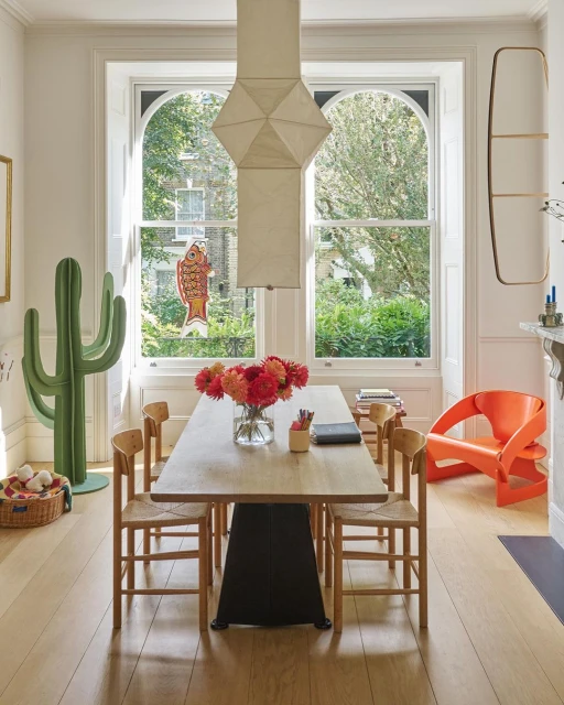 Bright and airy dining room interior with a light wood table, mismatched chairs, and natural light from large windows. Home decor.