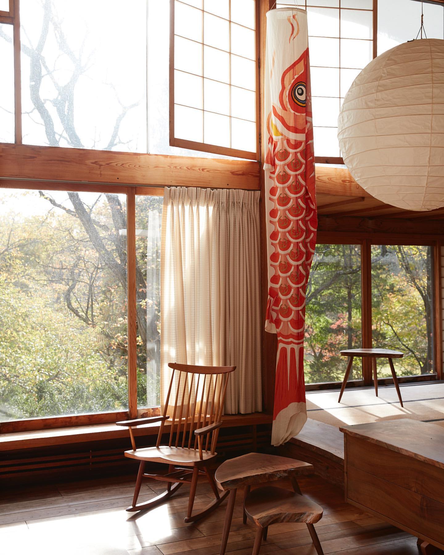 Wooden rocking chair and side tables in a home interior with large windows and a decorative fish windsock hanging from the ceiling.