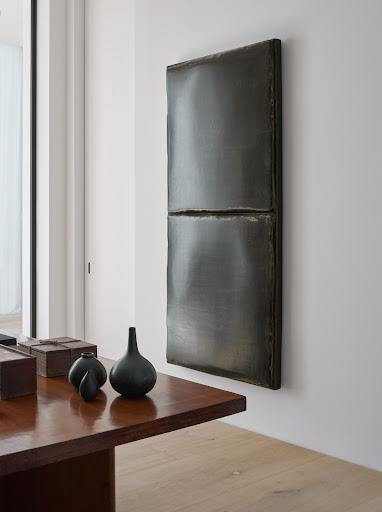 Abstract rectangular wall art hangs above a dark wood table with vases in a naturally lit interior space, showing home decor.