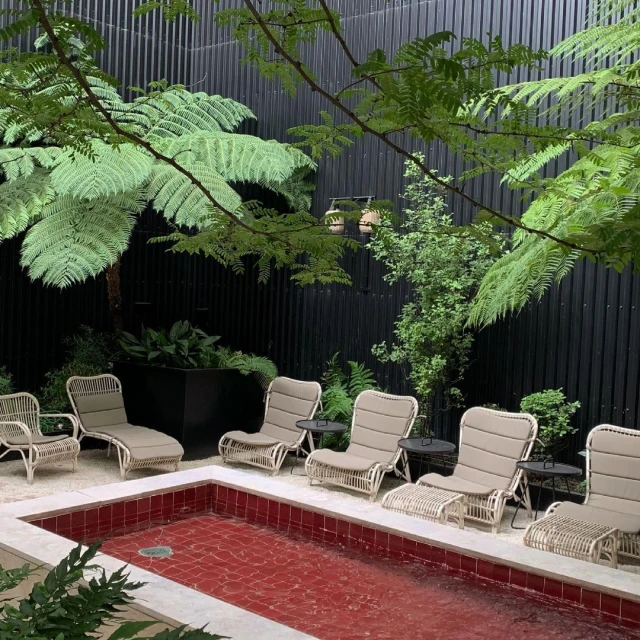 Outdoor relaxation area featuring wicker lounge chairs arranged around a small, tiled pool, surrounded by lush greenery and trees.