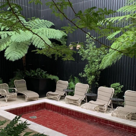 Outdoor relaxation area featuring wicker lounge chairs arranged around a small, tiled pool, surrounded by lush greenery and trees.