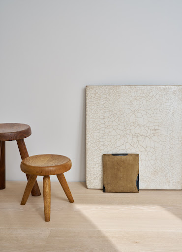 Wooden stools arranged near artwork on a light wood floor against a neutral wall, creating a simple and elegant interior scene.