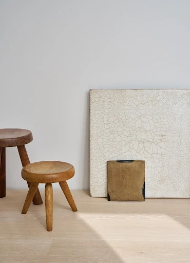 Wooden stools arranged near artwork on a light wood floor against a neutral wall, creating a simple and elegant interior scene.