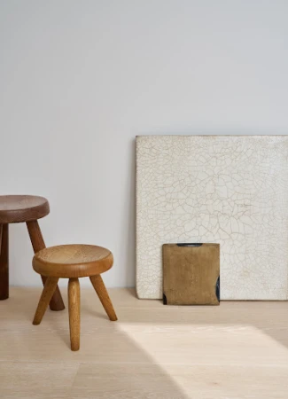 Wooden stools arranged near artwork on a light wood floor against a neutral wall, creating a simple and elegant interior scene.