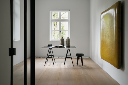 Minimalist interior featuring a modern table with decorative vases, a stool, and an abstract art piece in a bright, naturally lit room.
