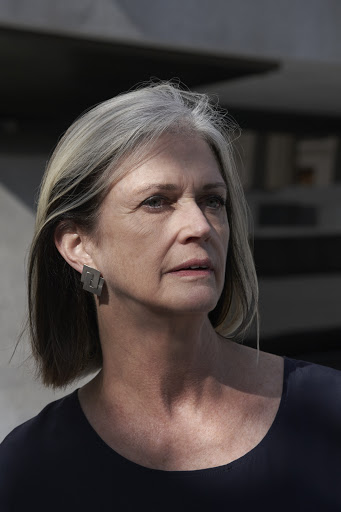 Portrait of a mature woman with short gray hair wearing an elegant navy blue dress in front of an airplane during the daytime.