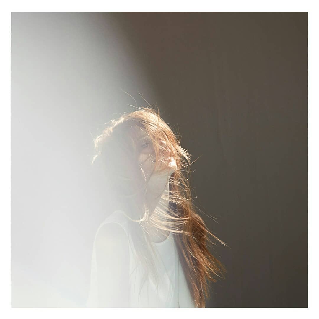 Woman with red hair wearing a white shirt against a grey background, illuminated by bright light shining from above.