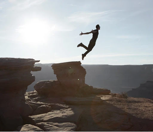 Silhouette of a man leaping between rocky cliff ledges against a pale sky captured by Martien Mulder