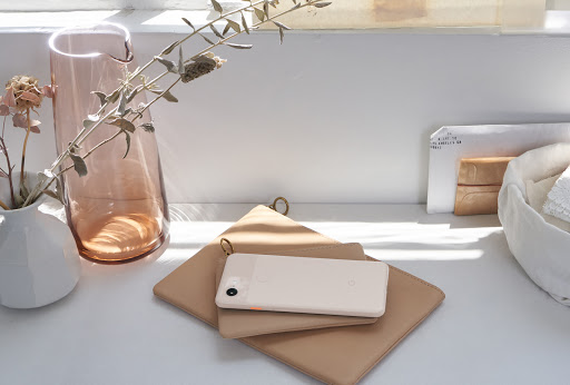 Minimalist product photography of a smartphone, vase, and floral arrangement on a white surface in front of a window.