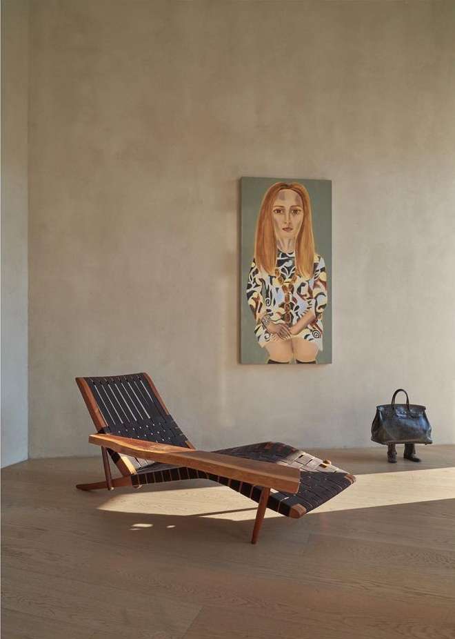 Modern interior showcasing a wooden lounge chair, painting of a woman, and a handbag with legs in a neutral colour palette.